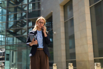 Fototapeta premium Professional businesswoman talking on phone holding tablet outdoors