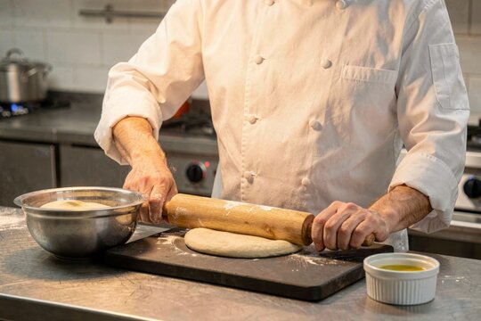 Chef using rolling pin to flatten dough for langos in modern kitchen, atmosphere cozy. Fried flatbread with sour cream cheese showcases culinary skills and fresh ingredients.