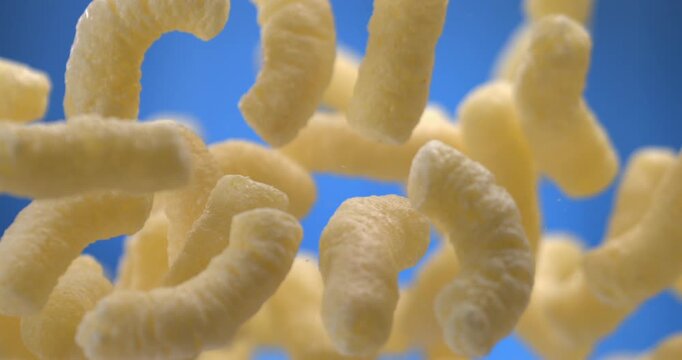 Corn sticks cheese puffs floating in the air on blue background slow motion