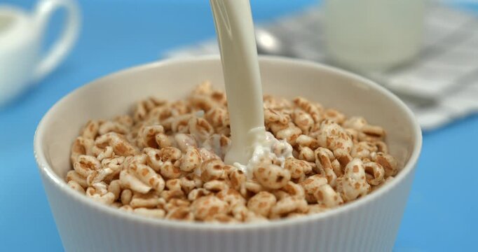 Milk pouring into crispy puffed honey wheat cereal in bowl creating dramatic splash in super slow motion