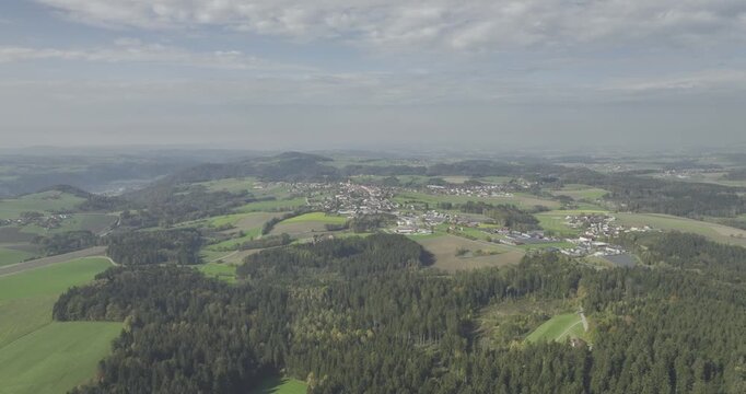 Drohnenaufnahme einer niederbayerischen Landschaft mit gr&uuml;nen W&auml;ldern, Feldern, H&uuml;geln, kleinen Ortschaften und weitem Ausblick unter bew&ouml;lktem Himmel.