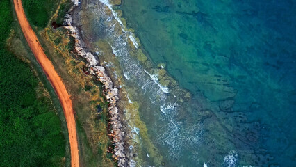A stunning coastline with vibrant blue waves crashing against rocky shores, lush green vegetation contrasting with a reddish-brown path. © wkproduction
