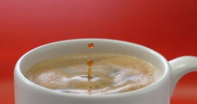 Coffee drop creating a splash and ripple in crema red background super slow motion