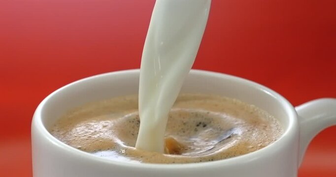 Cream pouring into coffee red background super slow motion