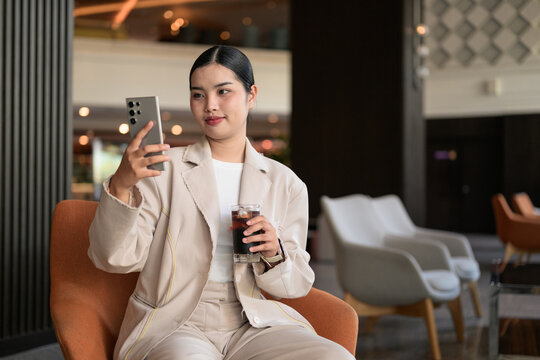 Young Thai Isan Woman Taking Selfie and Drinking Iced Coffee in Hotel Lobby Copy Space