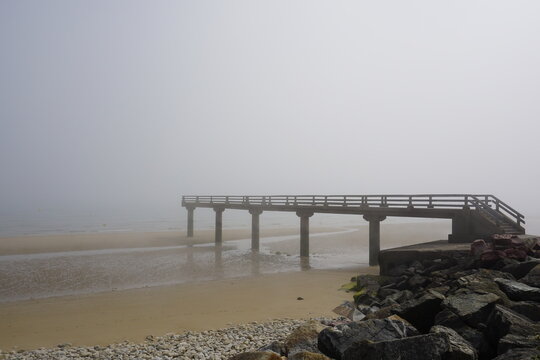 Embarcadero de hormig&oacute;n en playa con niebla en costa Normand&iacute;a con marea baja