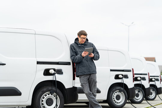 Fleet manager with digital tablet supervising rows of white electric delivery vans