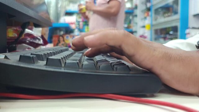 Side view of hands typing on a black computer keyboard at a retail shop or grocery store counter, billing and checkout concept