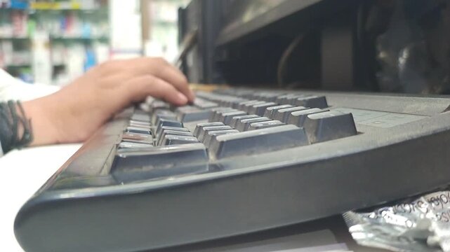 Side view of a person typing on a computer keyboard in an office or shop, data entry and daily business operations concept