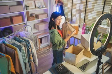 Fototapeten Restaurant Happy Asian woman looking at camera live streaming fashion clothing sales, online retail e-commerce entrepreneur, social commerce influencer web broadcasting and modern digital side hustle concept  © whyframeshot