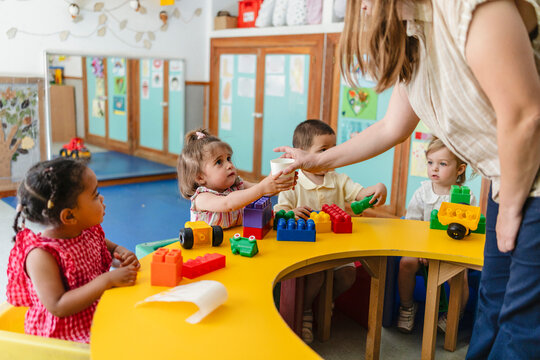 Caregiver providing water to diverse children in nursery classroom
