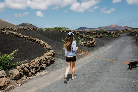 Woman walking a dog through Lanzarote's volcanic vineyards