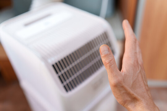 Man checking the freezing airflow from a running mobile AC unit during hot summer