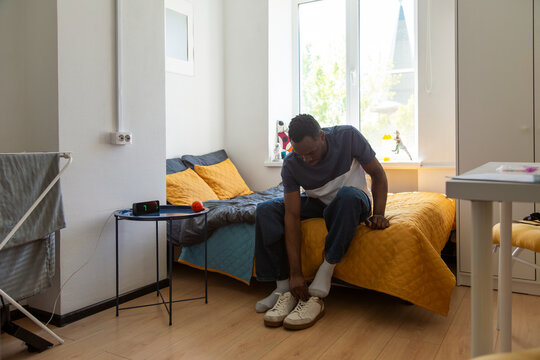 Student reading paper while sitting on bed in dormitory room