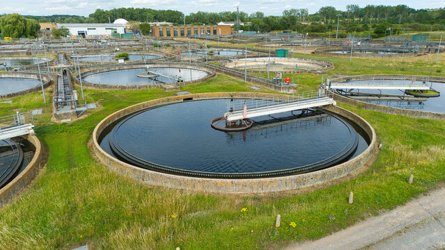 Aerial view of Thames Water Sewage Works featuring large circular sedimentation tanks and industrial infrastructure surrounded by green fields in Hoddesdon, England, United Kingdom.