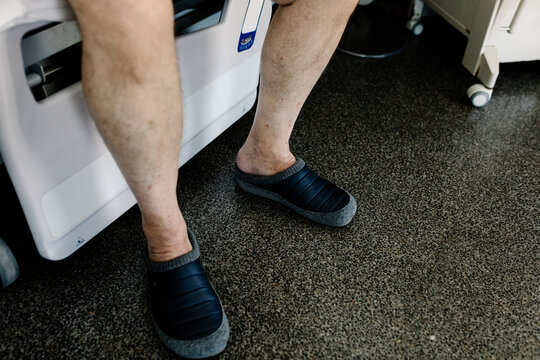 Unknown patient wearing slippers sits on the edge a hospital bed