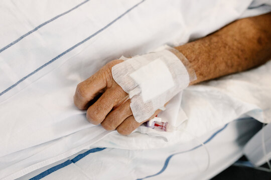 Close-up of a patient's hand resting on white hospital sheets