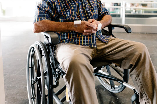 Older patient sits in wheelchair with folded hands outside a hospital