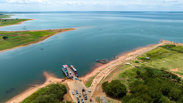 Aerial view of a ferry docked at a landing ramp on Lake Volta with vehicles waiting to board and small wooden boats along the shoreline in Kwahu Afram Plains South, Eastern Region, Ghana.