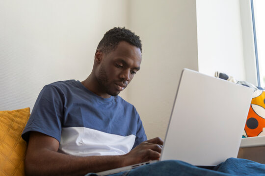Student using laptop while sitting on bed in dormitory room