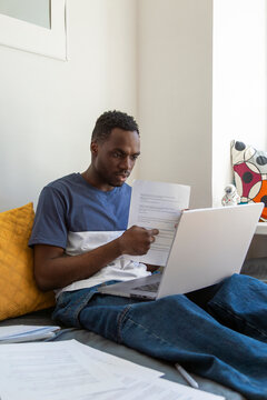 Man reviewing documents on bed with laptop at home