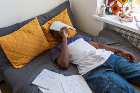 Student lying on bed feeling stressed while studying in dormitory