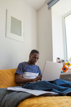 Student working on laptop in bed in minimalist dormitory room