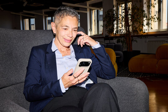 Ederly woman sits in a corporate lobby, using her smartphone