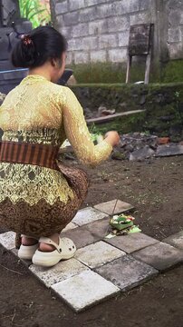 Balinese Woman is performing Traditional Offering Ritual or Worship Ritual at home during Kuningan Ceremony in Bali. Religion, Culture, and Travel Concept. 4K Footage