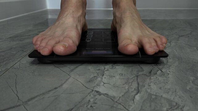 A man stands barefoot on an electronic floor scale to check his weight