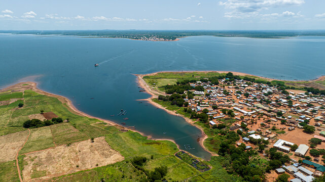Aerial view of a village situated on the shores of Lake Volta, featuring small houses, surrounding agricultural fields, and boats on the water in Kwahu Afram Plains South, Eastern Region, Ghana.