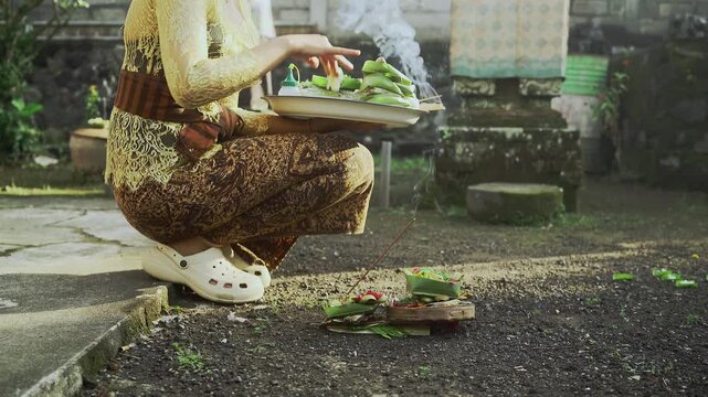 Balinese Woman is performing Traditional Offering Ritual or Worship Ritual at home during Kuningan Ceremony in Bali. Religion, Culture, and Travel Concept. 4K Footage