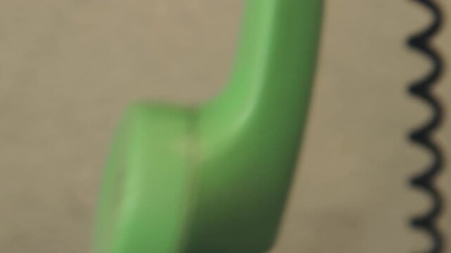 Detailed close-up shot of green telephone receiver handset dangling from its coiled cord. The vintage rotary phone plastic surface with speaker holes. Part of outdated analog communication technology