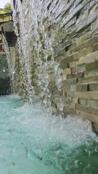 Water cascades down stone wall into clear pool below
