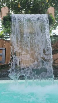 Water falls down stone into bright blue pool surrounded by greenery