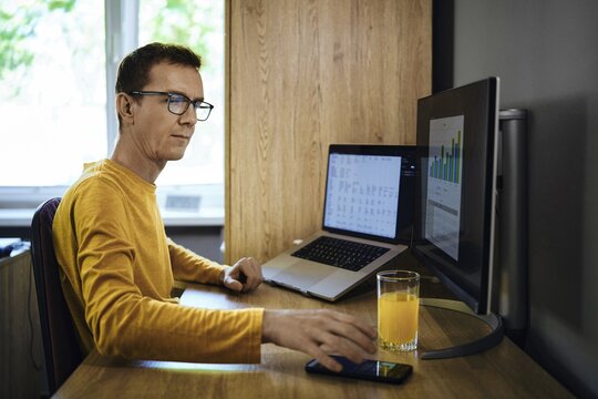 A man in a yellow shirt sits at a desk in a home office. He was distracted from studying statistics by a phone call