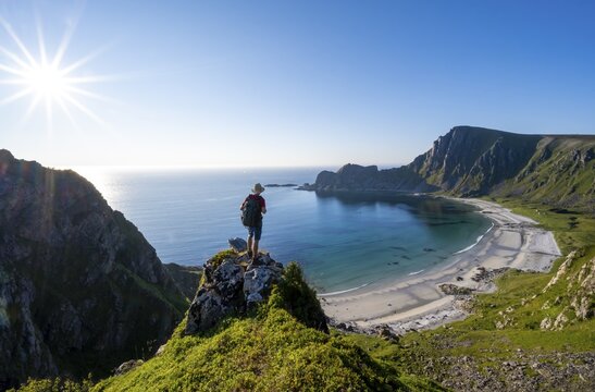 Mountaineer with view of coastal landscape, steep coast with summit M&aring;tind or M&aring;tinden, H&oslash;yvika beach and sea, hike to the summit of M&aring;tind, Sun Star, And&oslash;ya Island, Vester&aring;len, Nordland, Norway
