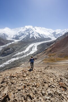 Mountaineer at Traveller's Pass with view of impressive mountain landscape, high mountain landscape with glacier moraines and glacier tongues, glaciated and snow-covered mountain peaks, Lenin Peak and Peak of the XIX Party Congress of the CPSU, Trans Alay Mountains, Pamir Mountains, Osh Province, Kyrgyzstan