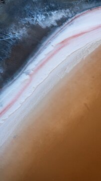 Aerial view of the salt lake with vibrant orange water, white salt crusts, and dark shoreline textures in Karlgarin, Western Australia, Australia.