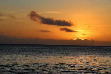 Fototapeta premium Beautiful ocean sunrise with a golden orange sky and dramatic clouds over the calm water surface. seascape background banner.