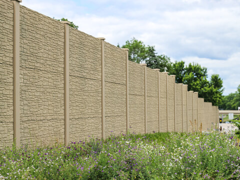 Concrete noise barrier wall with a faux stone texture next to a grassy highway roadside. infrastructure concepts