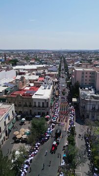 Aerial drone view of a traditional parade moving along an avenue toward the cathedral during the Feria de San Marcos in Aguascalientes, Mexico.