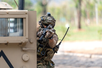 Fototapeta premium One army man point gun to enemy direction and lean on front left door of High Mobility Multipurpose Wheeled Vehicle to practice of fight with enemy.