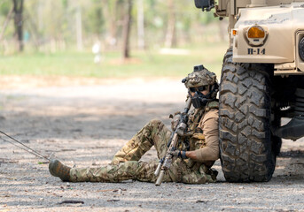 Fototapeta premium One army man sit and lean on right side front wheel of High Mobility Multipurpose Wheeled Vehicle to practice of fight with enemy.