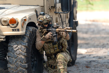 Fototapeta premium One army man sit and lean on left side front wheel of High Mobility Multipurpose Wheeled Vehicle and point the gun to enemy direction.