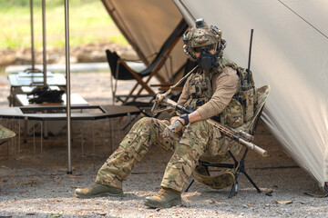 Fototapeta premium One army man or soldier sit on chair and hold his weapon in front of military tent with look at camera.