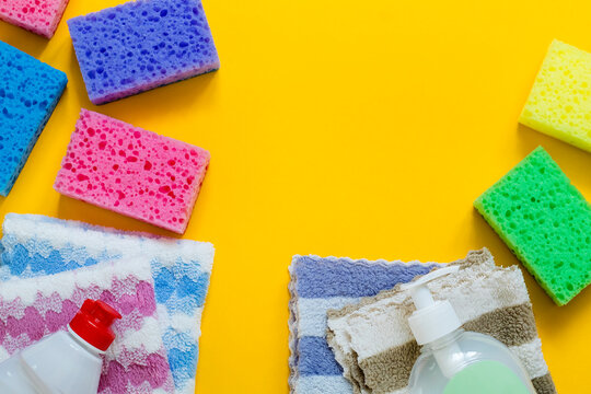 Colorful sponges, soft microfiber cloths, and cleaning liquid bottles neatly arranged on a bright yellow background with copy space.