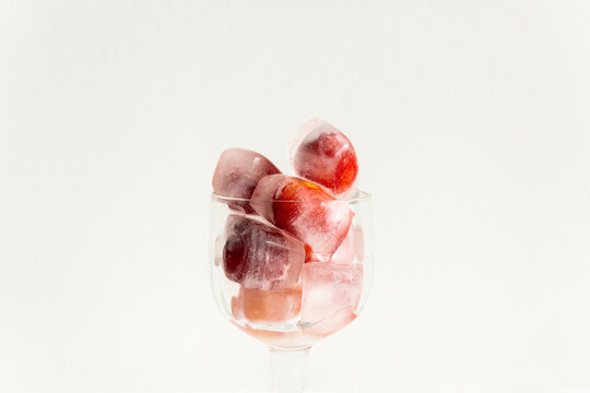 Gla&ccedil;ons avec des cerises rouges givr&eacute;es &agrave; l'int&eacute;rieur empil&eacute;s dans un verre sur pied transparent, vue de face en gros plan, arri&egrave;re-plan blanc
