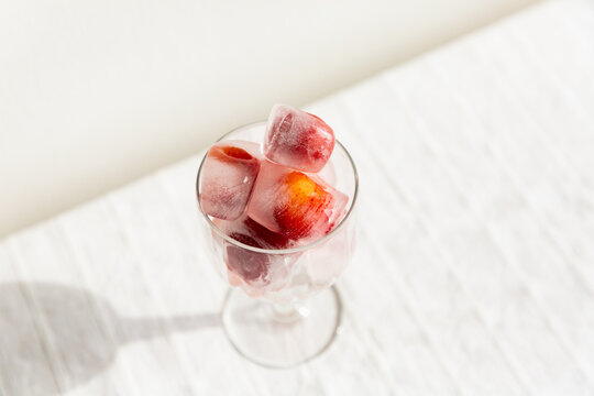 Verre sur pied transparent rempli de gla&ccedil;ons avec des cerises rouges gel&eacute;es &agrave; l'int&eacute;rieur, pos&eacute; sur une nappe blanche, vue trois-quart du dessus, sensation rafra&icirc;chissante