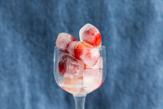 Verre transparent rempli de gla&ccedil;ons avec des cerises rouges givr&eacute;es &agrave; l'int&eacute;rieur, gla&ccedil;ons empil&eacute;s, vue de face en gros plan, arri&egrave;re plan bleu, d&eacute;salt&eacute;rant